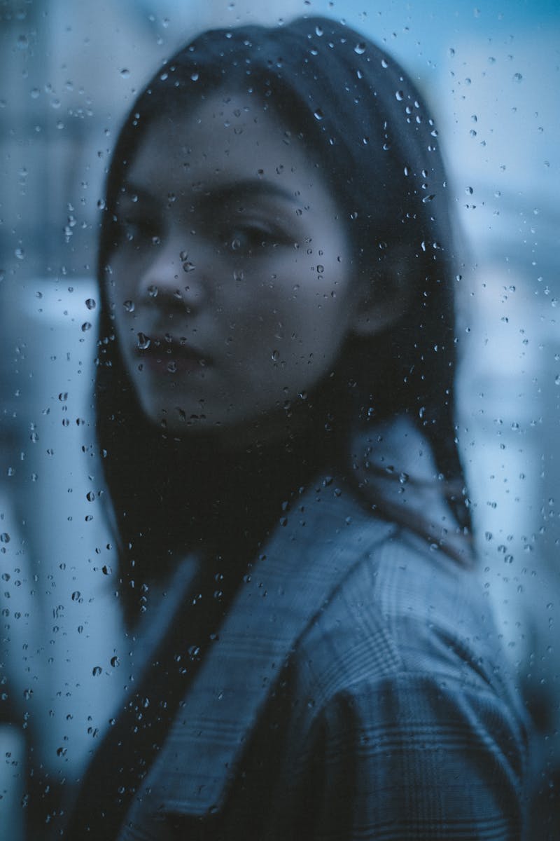 Thoughtful teen looking through rainy window